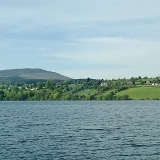Camlough Lake with fields and houses on the far shore and a rounded hill behind