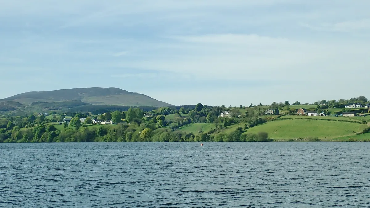Camlough Lake with fields and houses on the far shore and a rounded hill behind