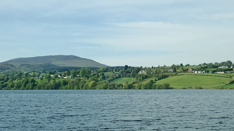 Camlough Lake with fields and houses on the far shore and a rounded hill behind