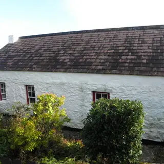 The whitewashed single storey farmhouse of the Grant ancestral homestead behind a garden of shrubs