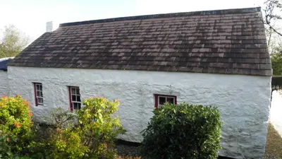 The whitewashed single storey farmhouse of the Grant ancestral homestead behind a garden of shrubs
