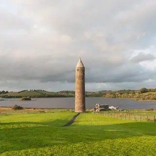 The round tower on Devenish Island standing over green grass with Lough Erne behind it