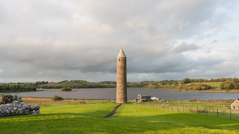 The round tower on Devenish Island standing over green grass with Lough Erne behind it