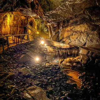 A lit walkway running beside dark water between cave walls and hanging formations in the Marble Arch Caves