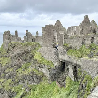 The ruined walls of Dunluce Castle on its cliff above the sea, with the stone bridge leading across