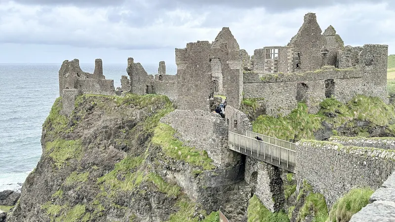 The ruined walls of Dunluce Castle on its cliff above the sea, with the stone bridge leading across