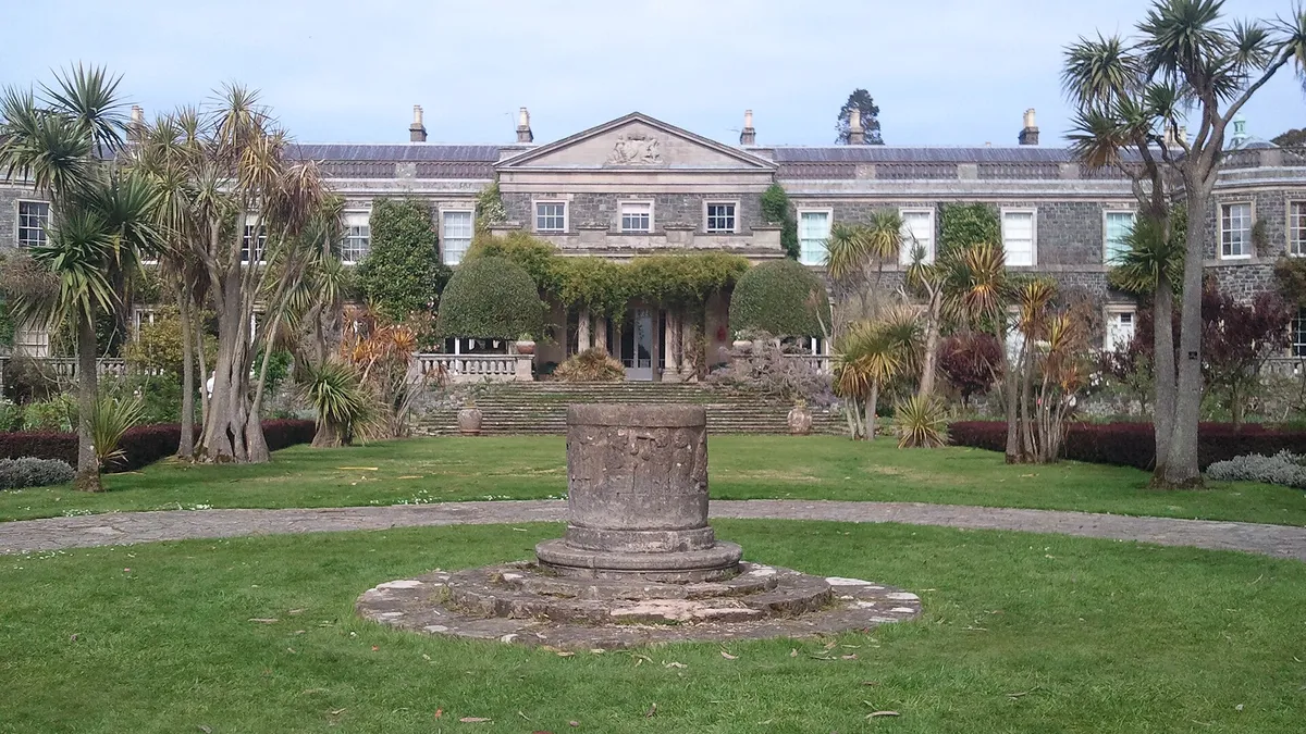 The front of Mount Stewart house behind a lawn with palms and a stone sundial