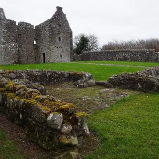 The roofless stone house of Tully Castle behind the low walls of its bawn