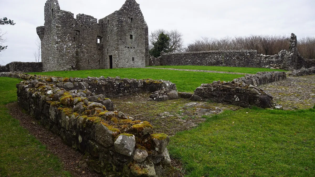 The roofless stone house of Tully Castle behind the low walls of its bawn