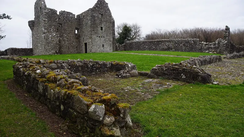 The roofless stone house of Tully Castle behind the low walls of its bawn