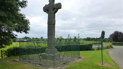 The tall carved high cross at Ardboe inside a low railing on a green